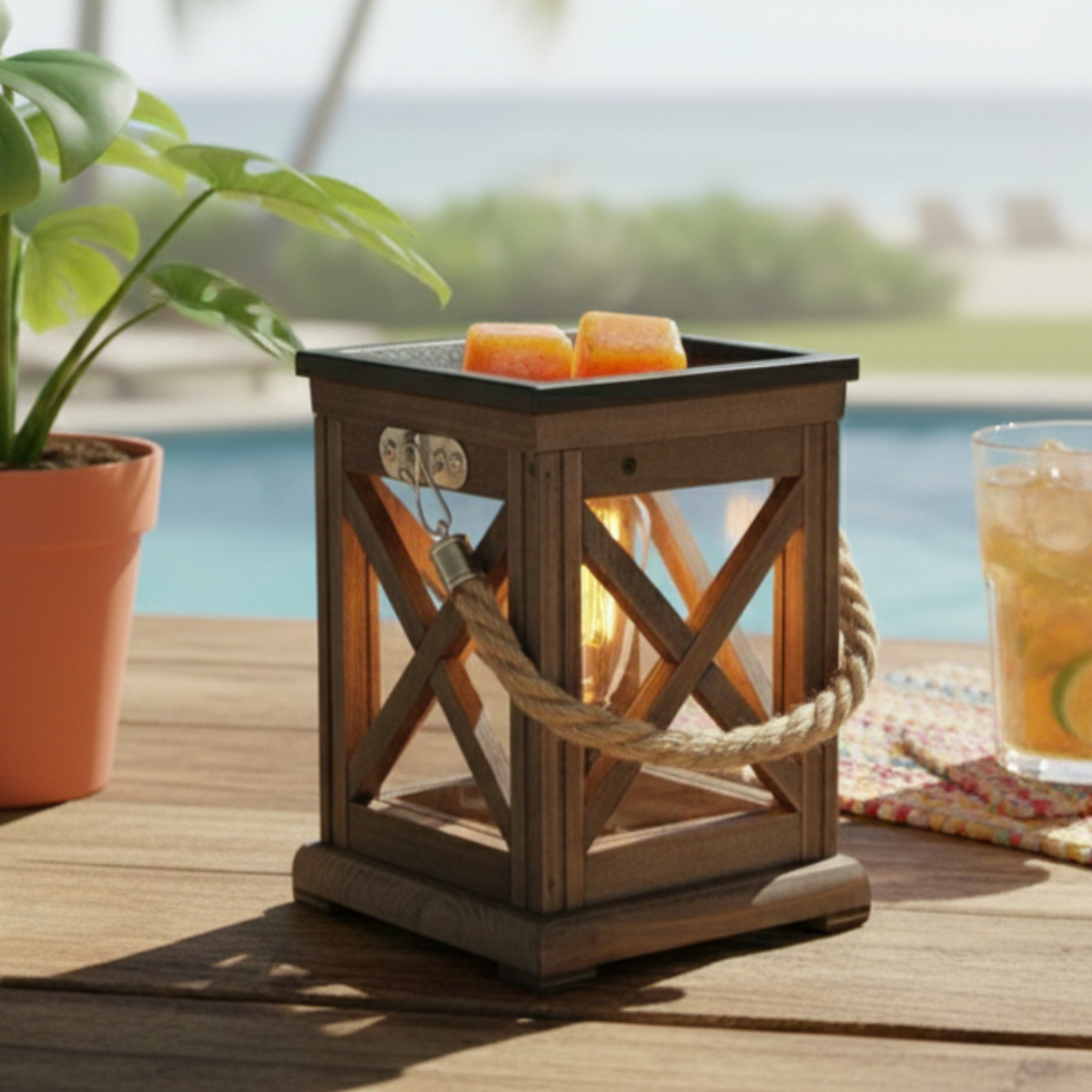 Wooden lantern wax warmer with Brazilian Beach Vibes Cubes in the dish on a patio table by a poolside.