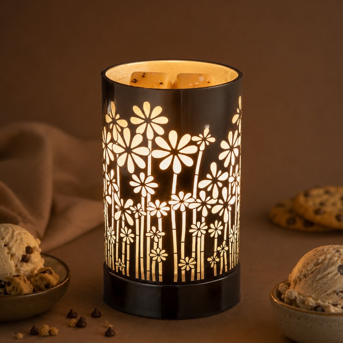 A wax melt warmer with floral pattern on a brown background with cookies and ice cream.