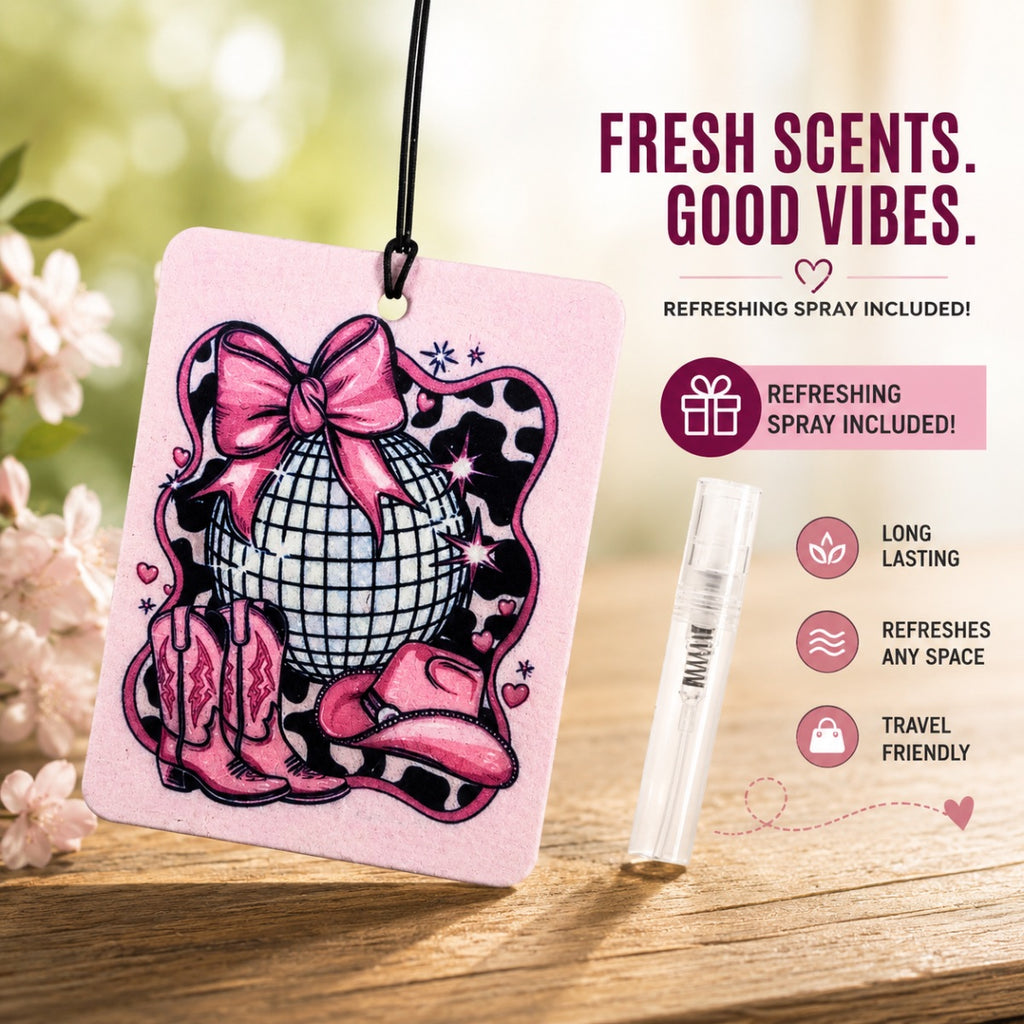 Pink air freshener with a disco ball and cowboy boots design, featuring a refreshing spray on a wooden surface with a blurred floral background.