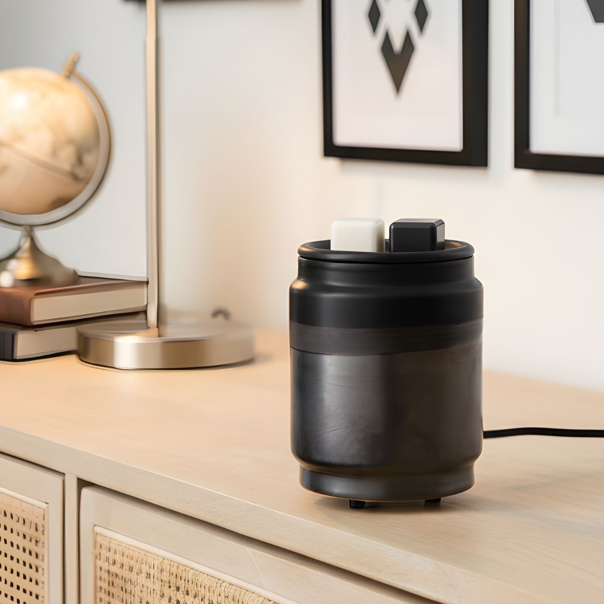 Black wax warmer with black and white wax cubes in it on a wooden surface with decorative items in the background.