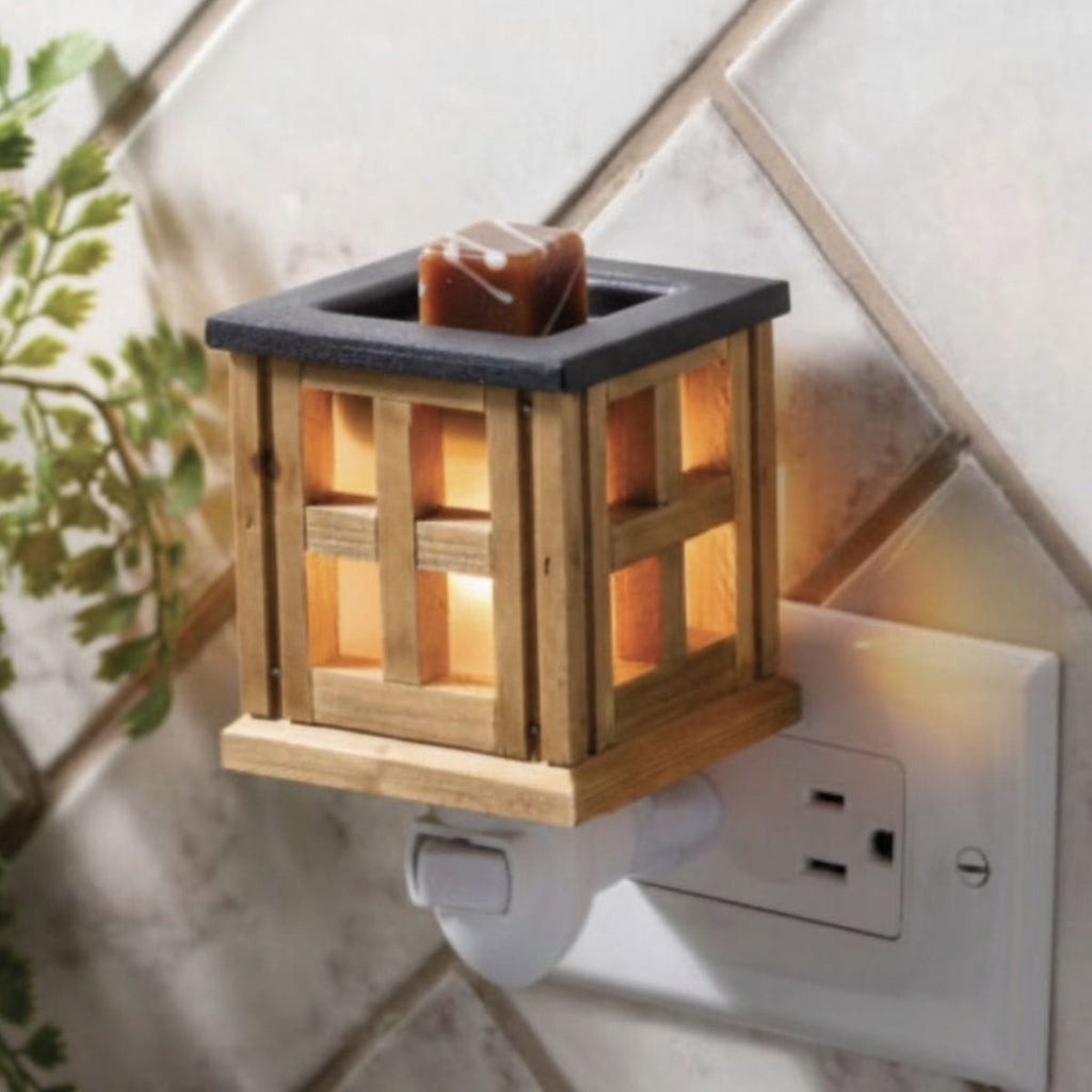 Wooden wax melt warmer illuminated and attached to an electrical outlet.