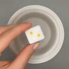 Hand holding a small white wax cube with yellow banana design on it against a gray background.