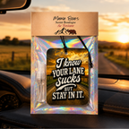 Mama Bears Scent Boutique air freshener package hanging on a car dashboard, featuring an iridescent holographic pouch with a black rectangular tag that reads 'I know YOUR LANE sucks BUT STAY IN IT.' and a small clear spray bottle.