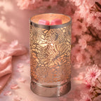 Decorative candle warmer with floral pattern on a soft pink background with flowers.