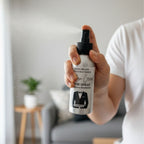 Person holding a Moden Creed room spray bottle in a living room setting.