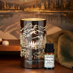 Diffuser oil/wax warmer with mountain design and a bottle of Calming Oasis diffuser oil on a wooden surface with a scenic background.