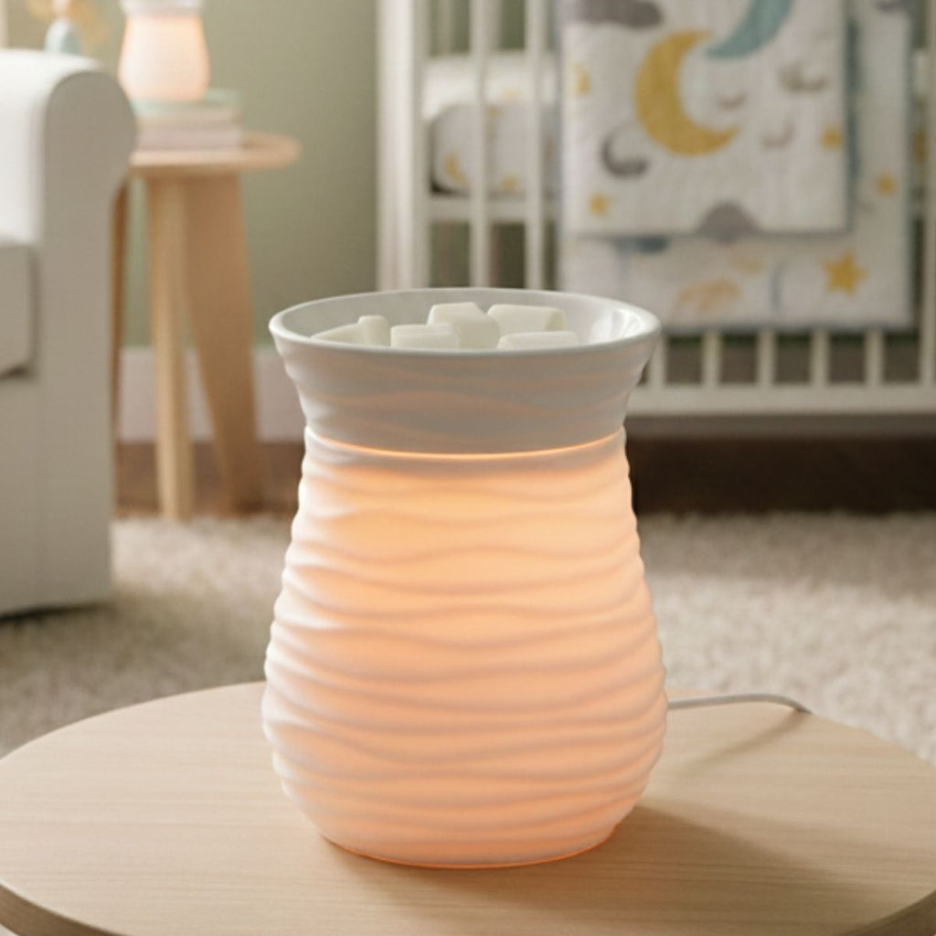 A White wax warmer lit up with white wax in the dish on a table in a nursery setting.