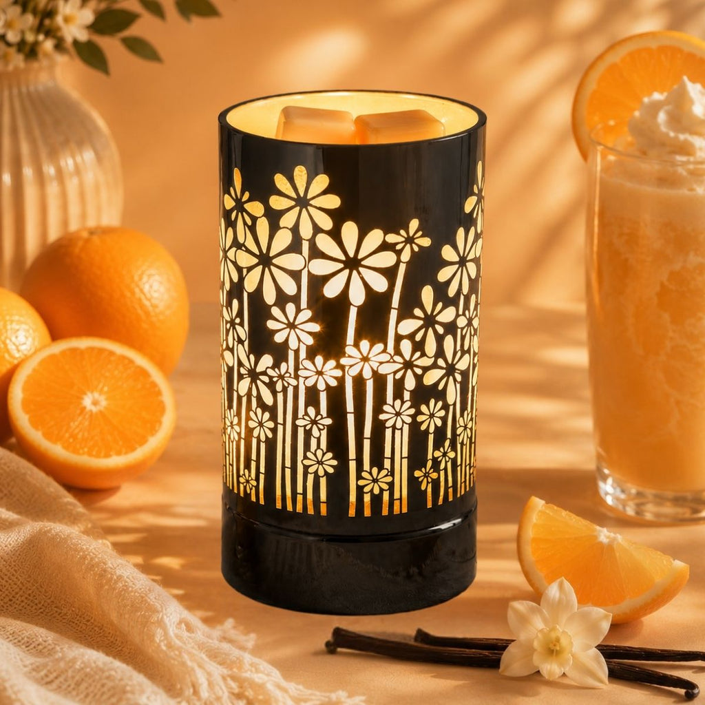 Decorative wax warmer with floral design on a table with oranges and a glass of juice.