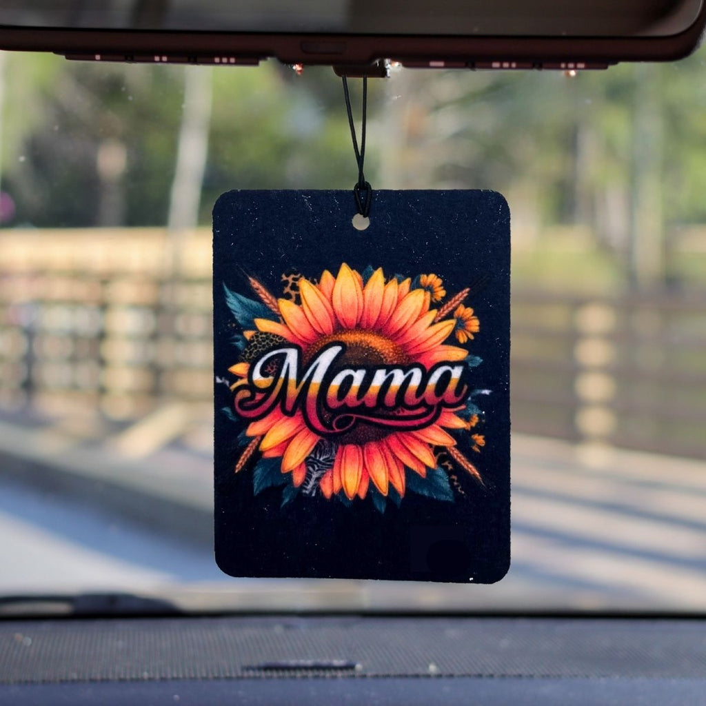 A felt air freshener hanging from a rear view mirror that has a picture of a sunflower on it and says the word Mama in the middle.