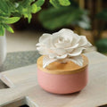 Decorative pink container with a white floral porcelain flower design on top, placed on a wooden surface.