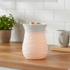 Two cubes of Saturday Morning Cartoons wax melts in a white textured wax warmer on a wooden surface with a blurred kitchen background.