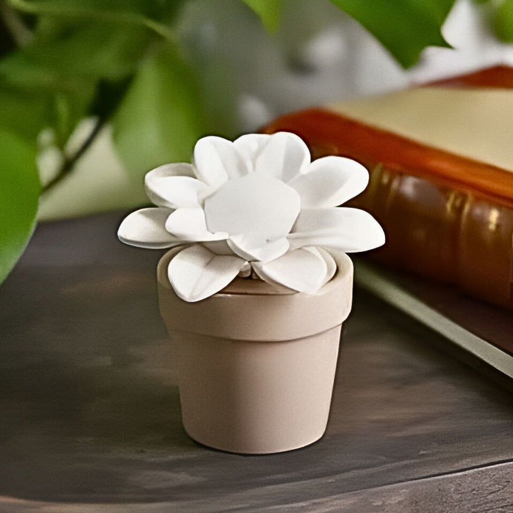 White ceramic sunflower in a beige pot on a wooden surface with greenery in the background