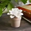 White ceramic sunflower in a beige pot on a wooden surface with greenery in the background
