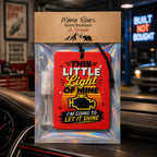 A red rectangular air freshener card with bold yellow and white text reading 'This Little Light of Mine I'm Going to Let It Shine' and a small clear spray bottle, packaged in an iridescent sleeve with a kraft header card labeled Mama Bears Scent Boutique Air Freshener. The product is photographed hanging on a car dashboard with a blurred nighttime street scene behind it.