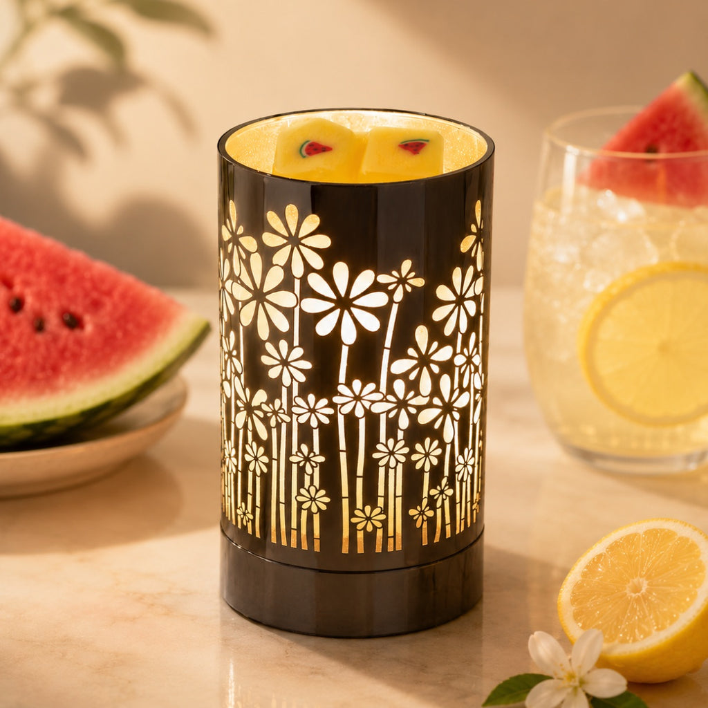 Decorative wax warmer with floral pattern on a table with fruit and a glass and two cubes of watermelon lemonade wax melts in the warmer.